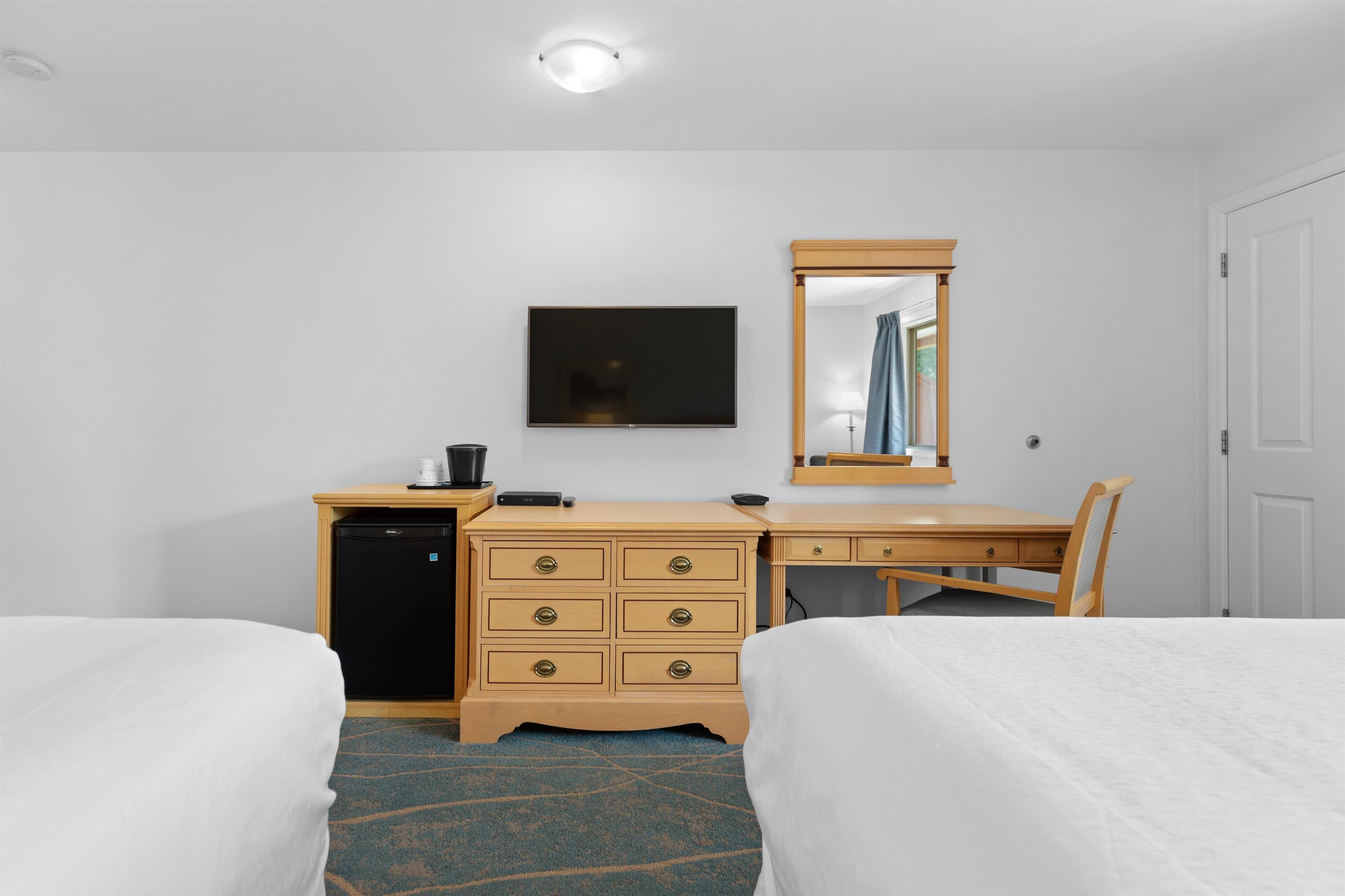A hotel room with two beds, a desk, a dresser, a television, and a mirror.