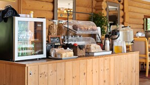 Un comptoir pour le petit-déjeuner avec un réfrigérateur, du pain, des viennoiseries et une machine à café, le tout dans un cadre rustique.