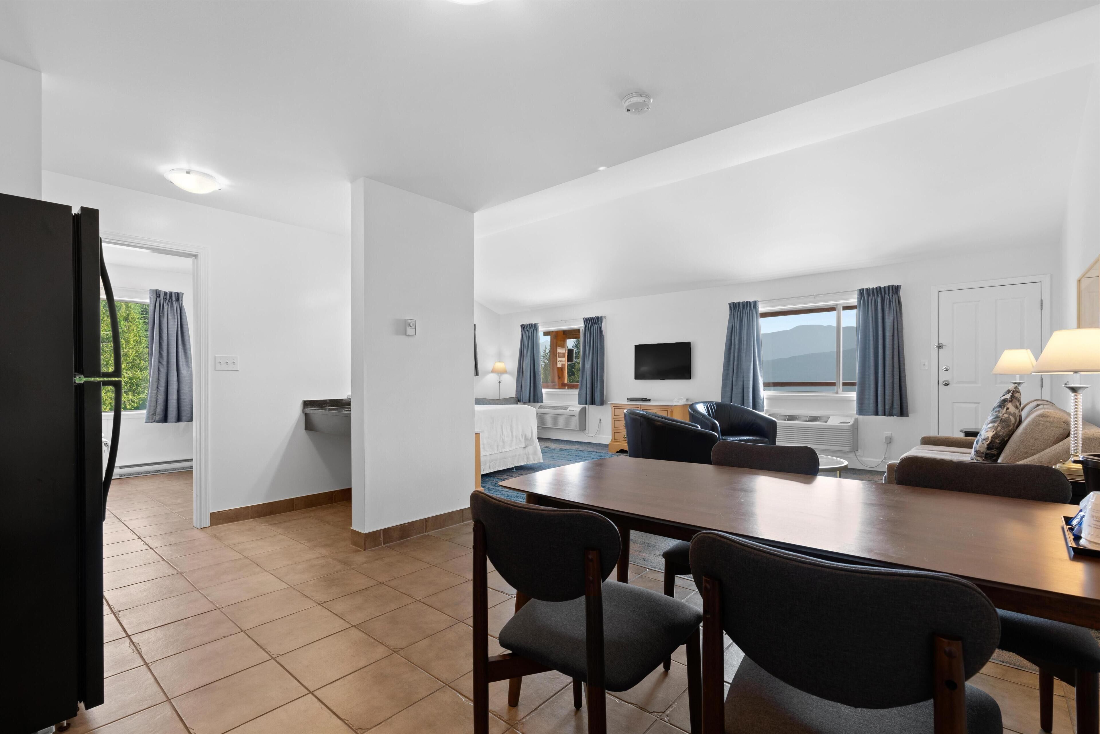 A modern hotel room with a dining area, a kitchen, and a living room.