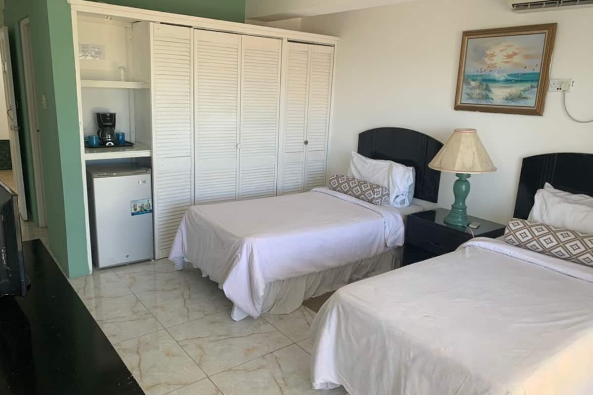 A hotel room with two beds, a wardrobe, a desk with a coffee maker, and a lamp.