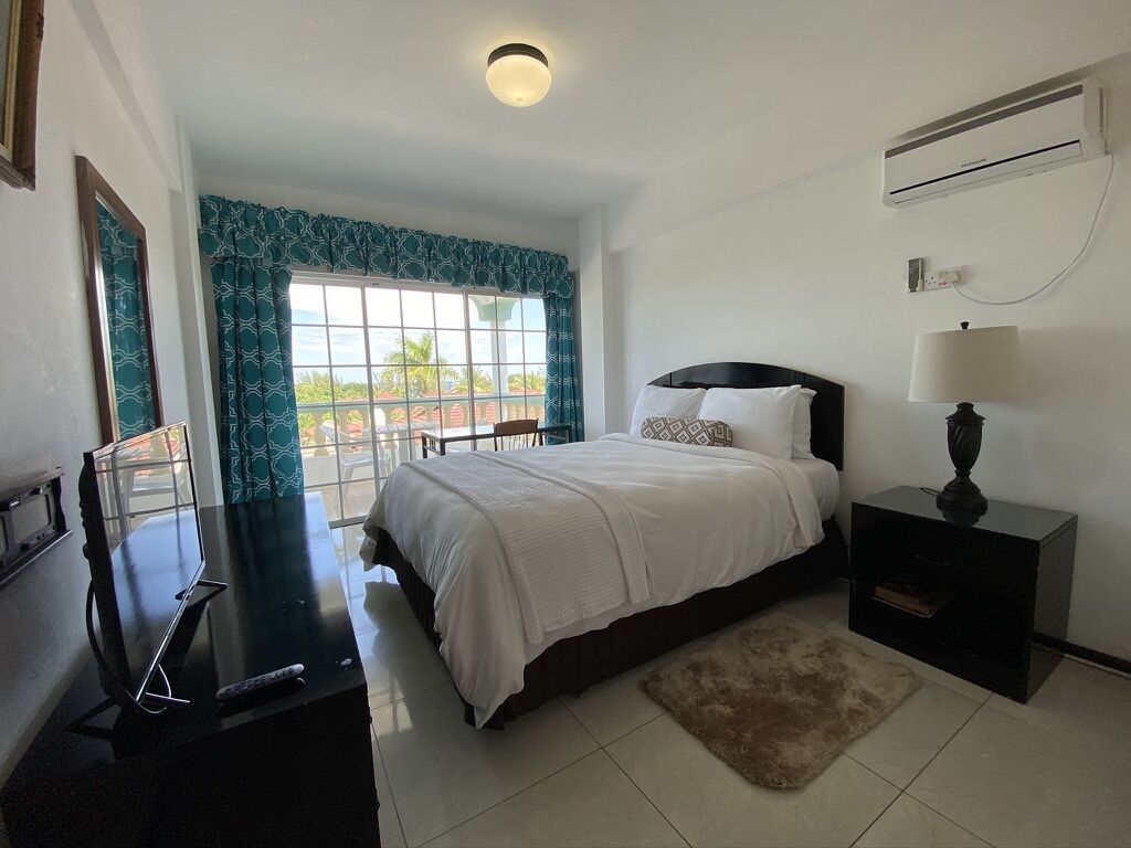 Una habitación de hotel con cama, televisión, lámpara y ventana con cortinas.