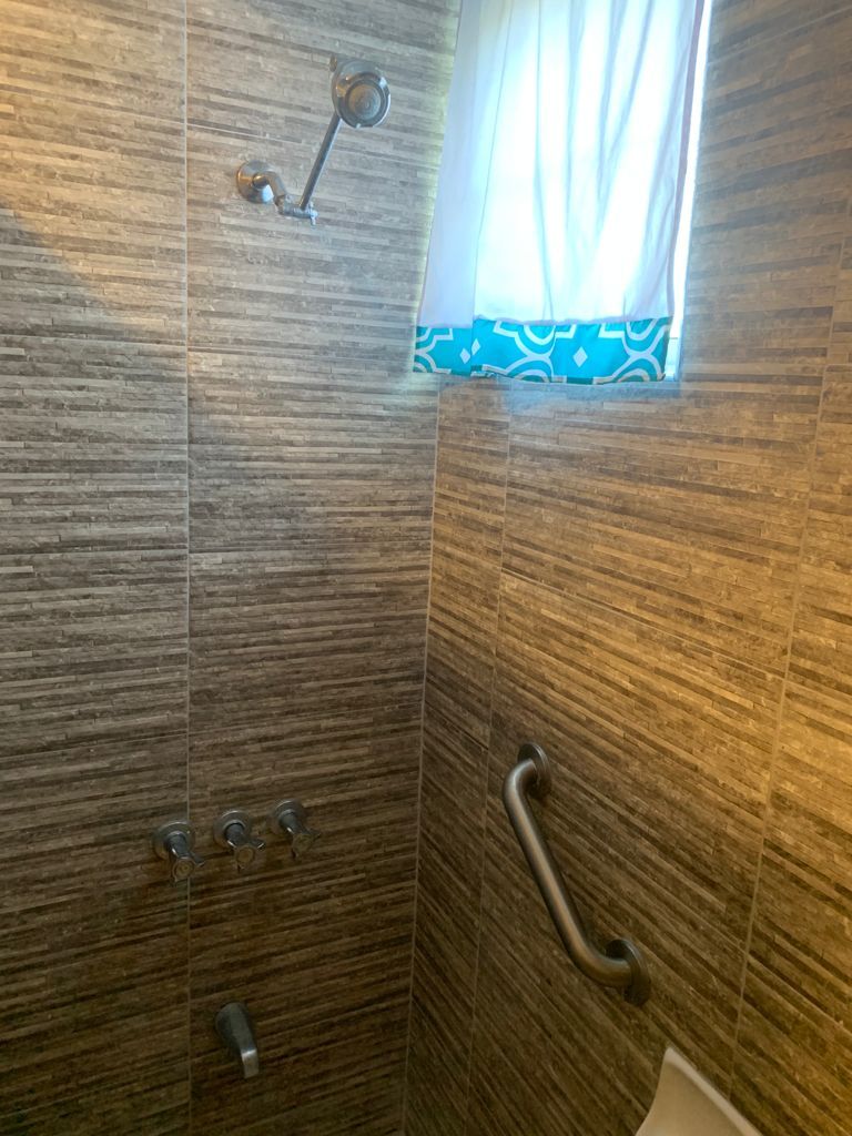 A shower with a handrail and a window with a patterned curtain.