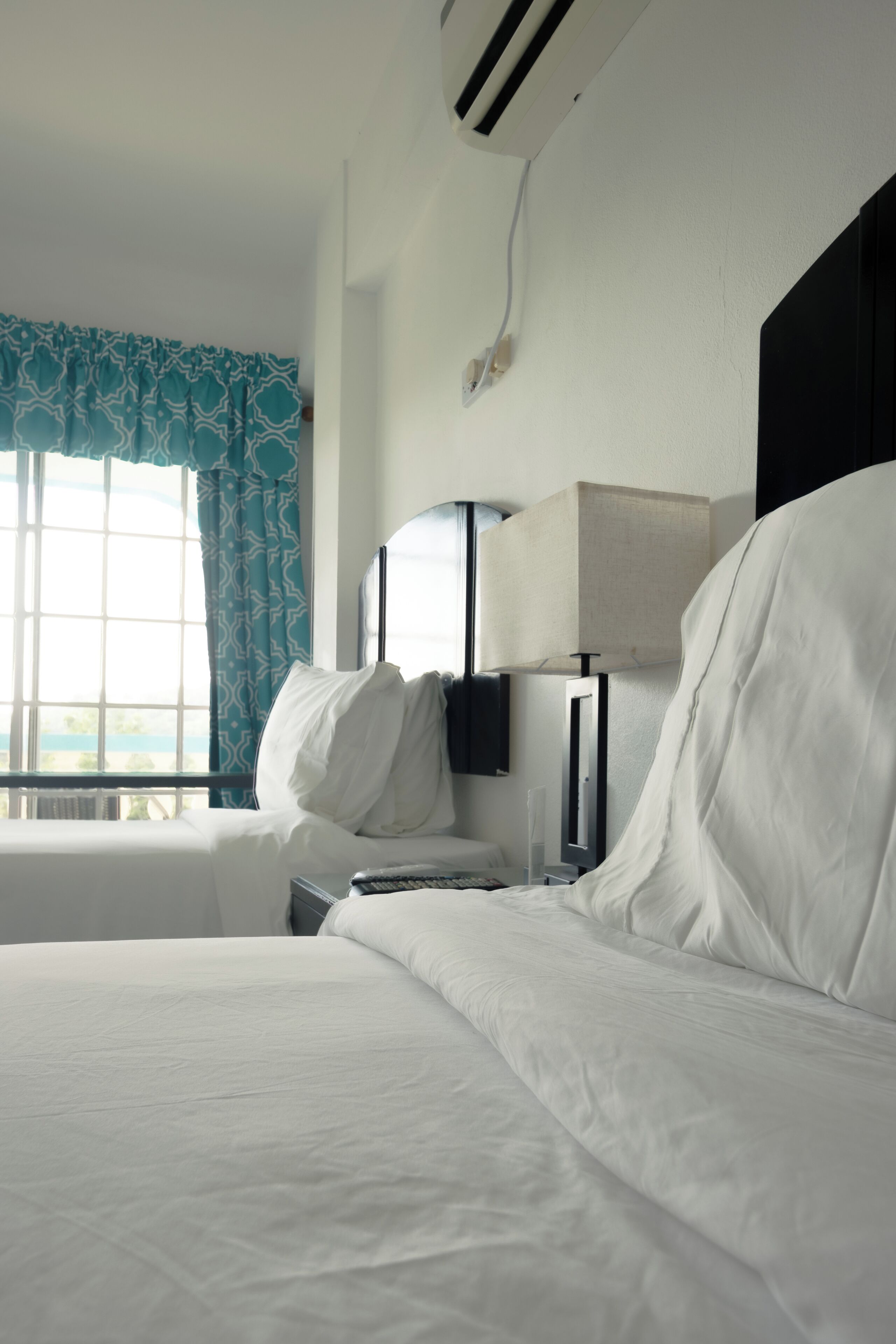 A hotel room with a bed, a bedside table, a lamp, and a window with curtains.