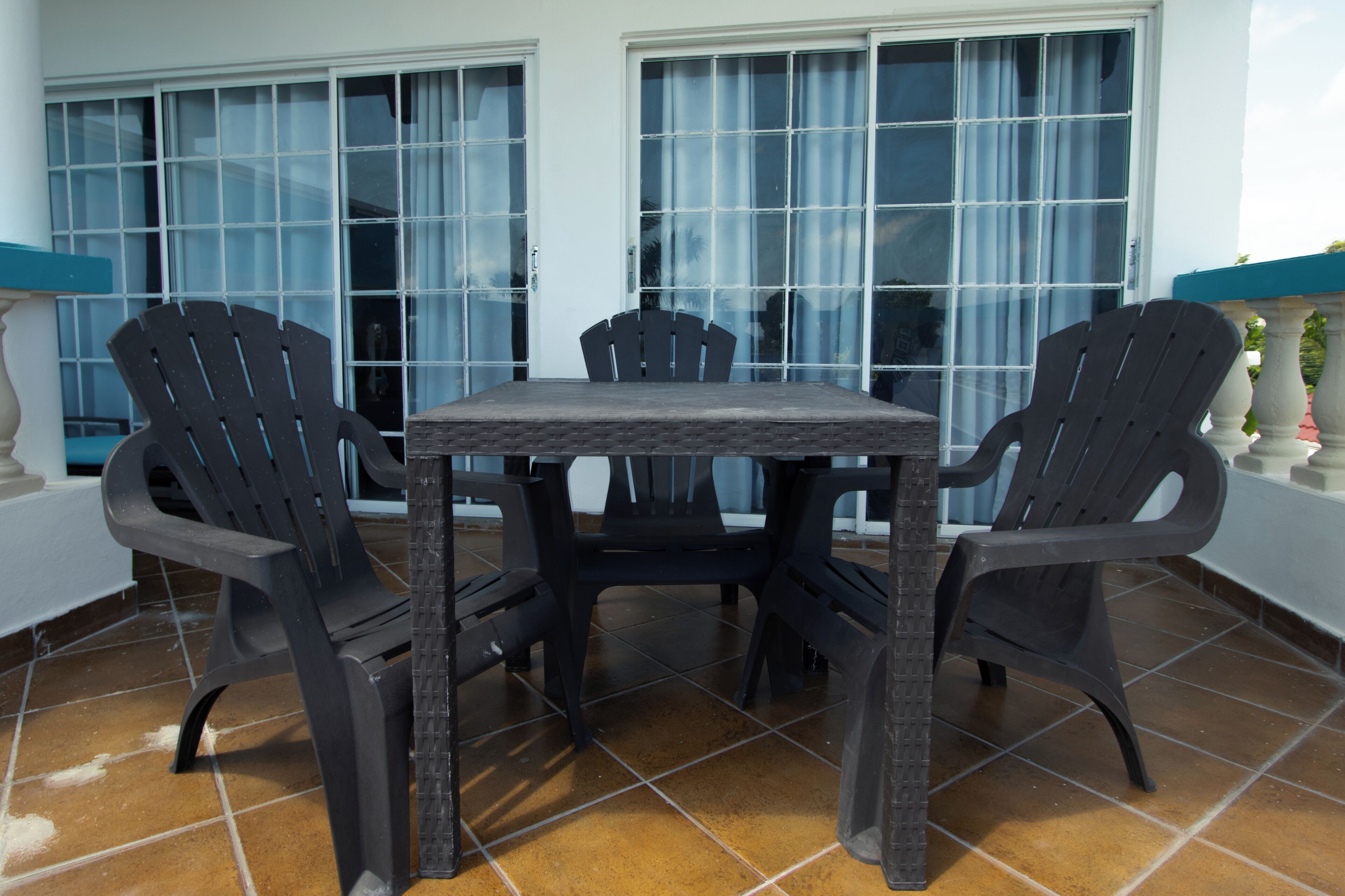 A patio area with a table and four chairs, large windows with curtains, and a tiled floor.
