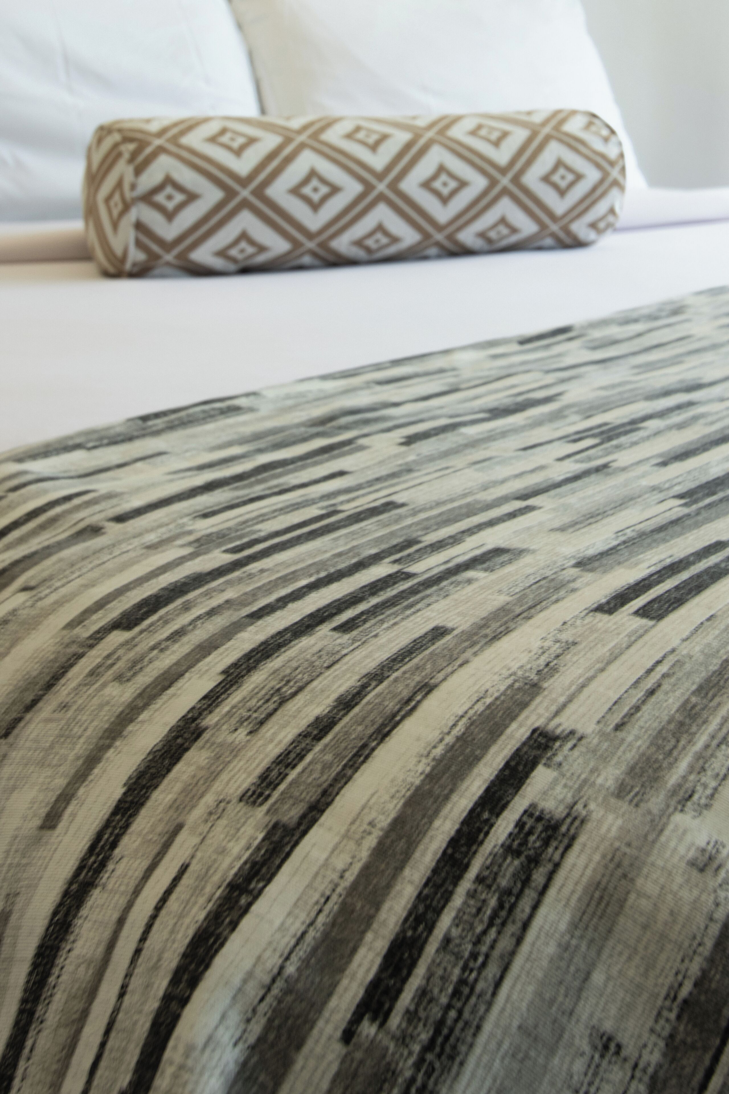 A close-up of a patterned pillow on a bed with a striped blanket.