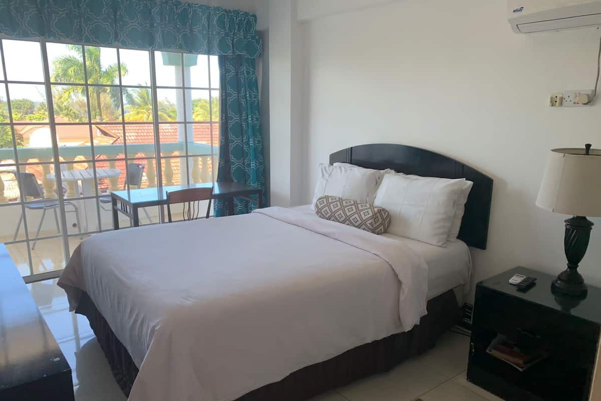 A hotel room with a bed, a nightstand with a lamp, a desk, and a view of the outside balcony.