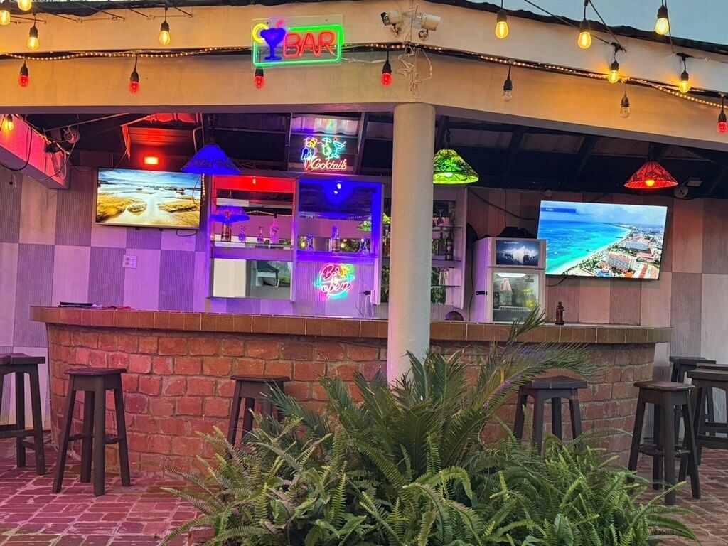 A bar with a neon sign, multiple screens, and outdoor seating.