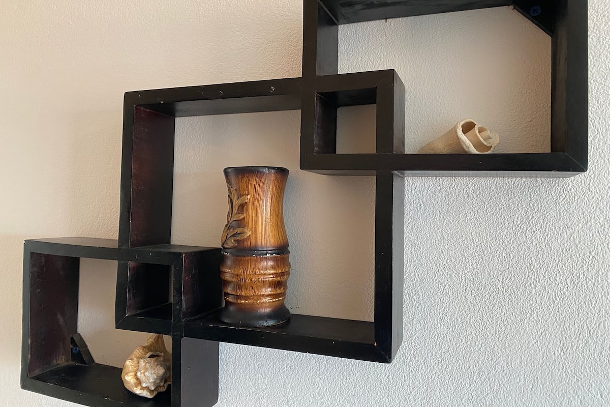 A wall-mounted black shelf unit with a decorative vase and a seashell.