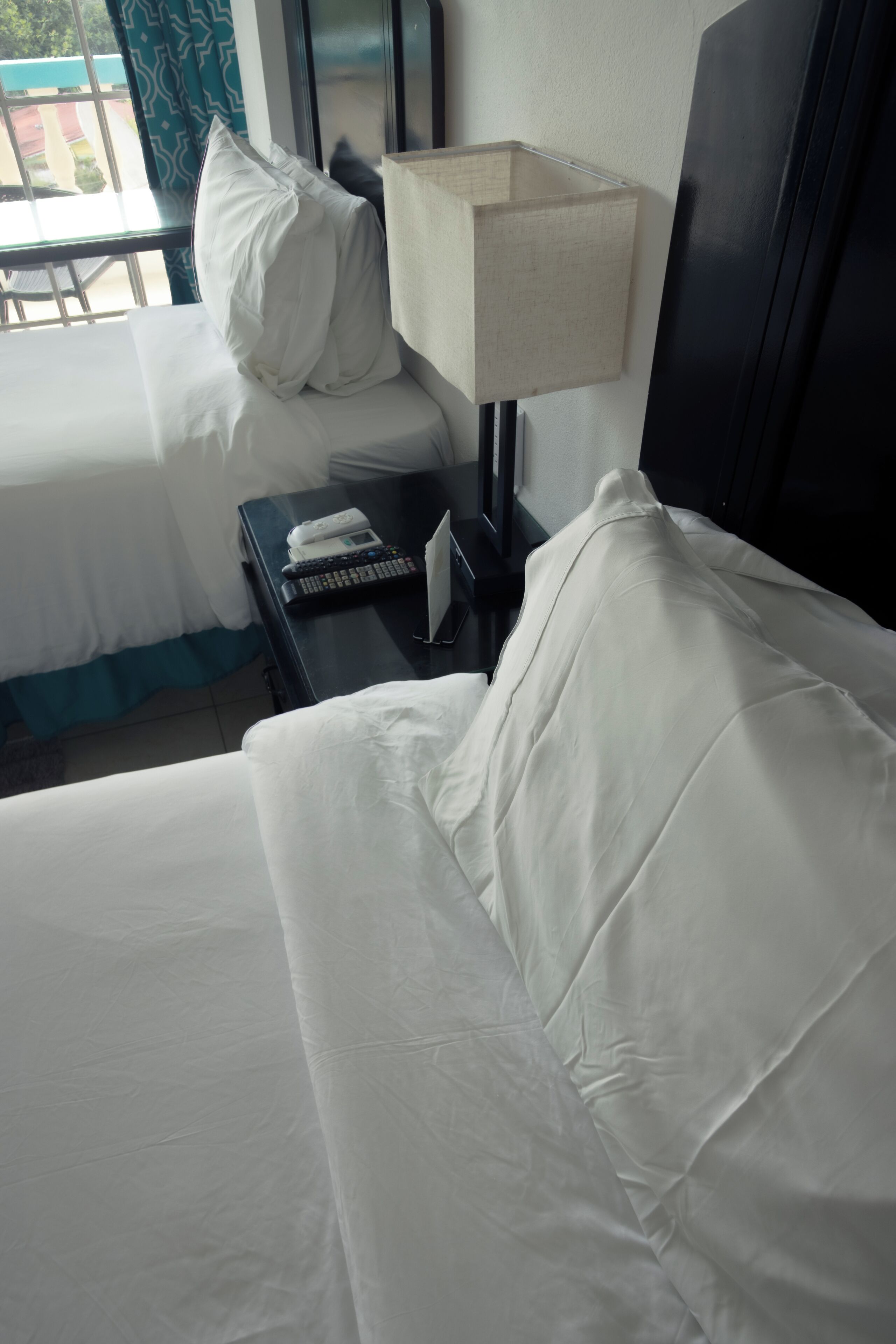 A hotel room with a bed, a nightstand with a lamp, a phone, and a window with curtains.