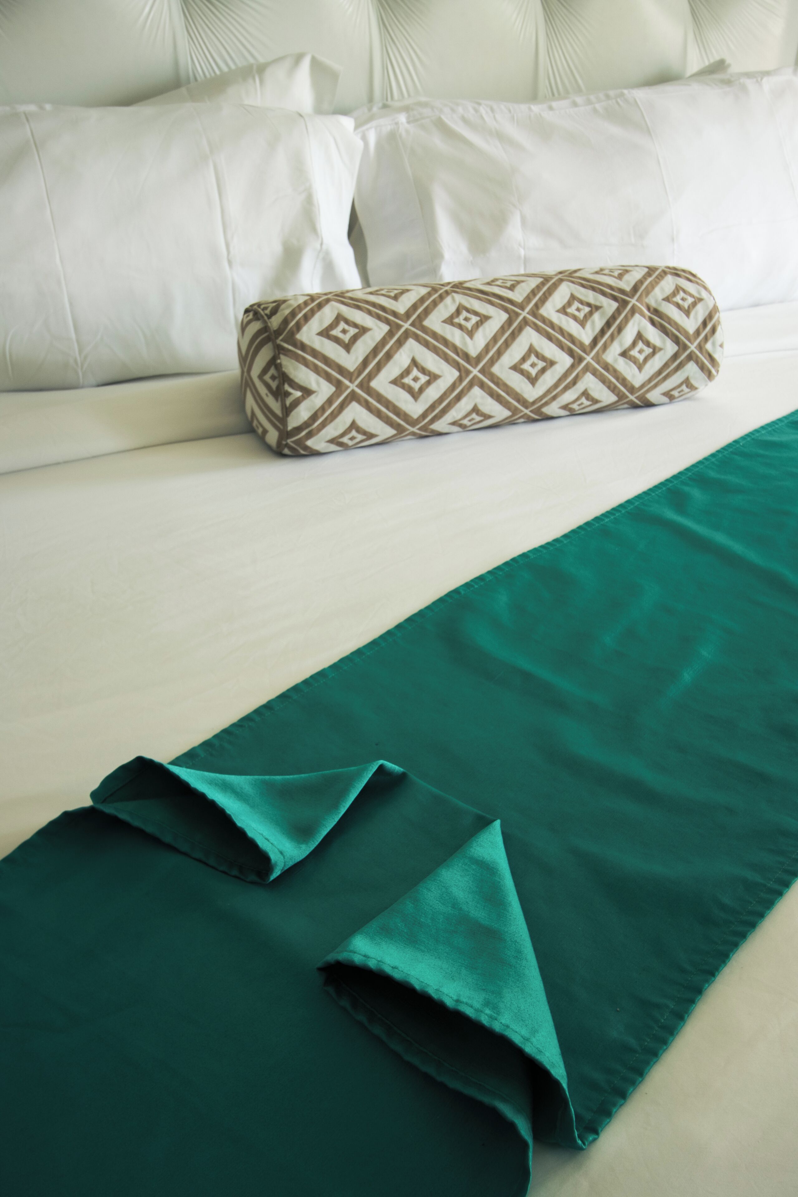 Una cama bien tendida con sábanas blancas y una manta verde.