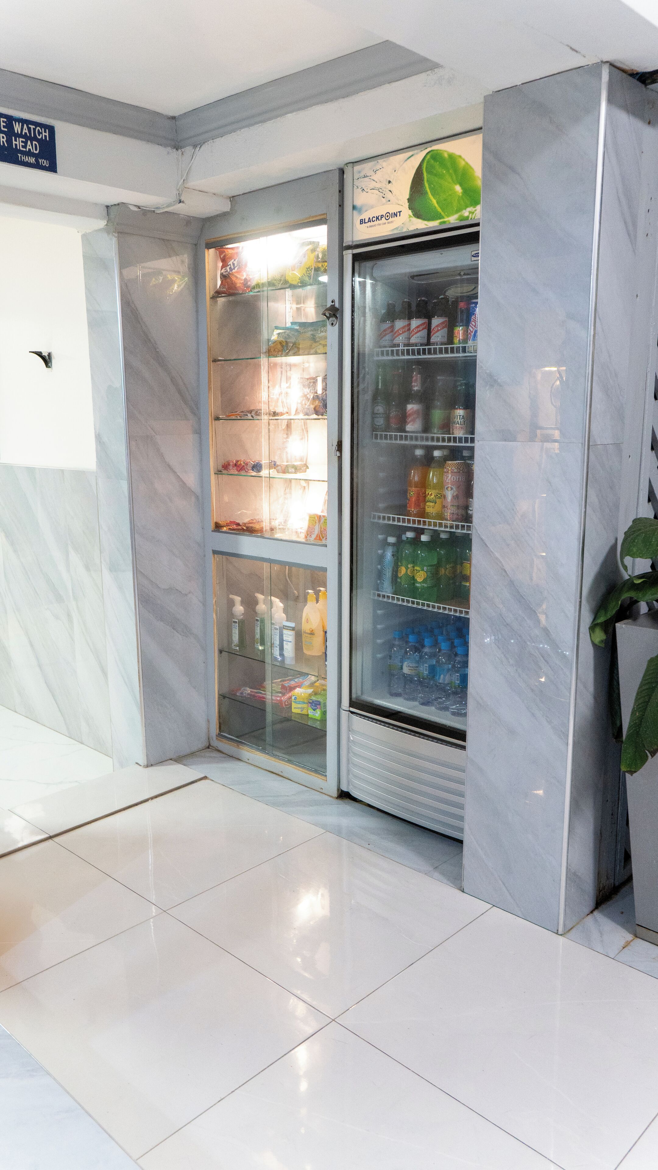 A vending machine with a variety of beverages and snacks, located in a clean, tiled area with marble walls.
