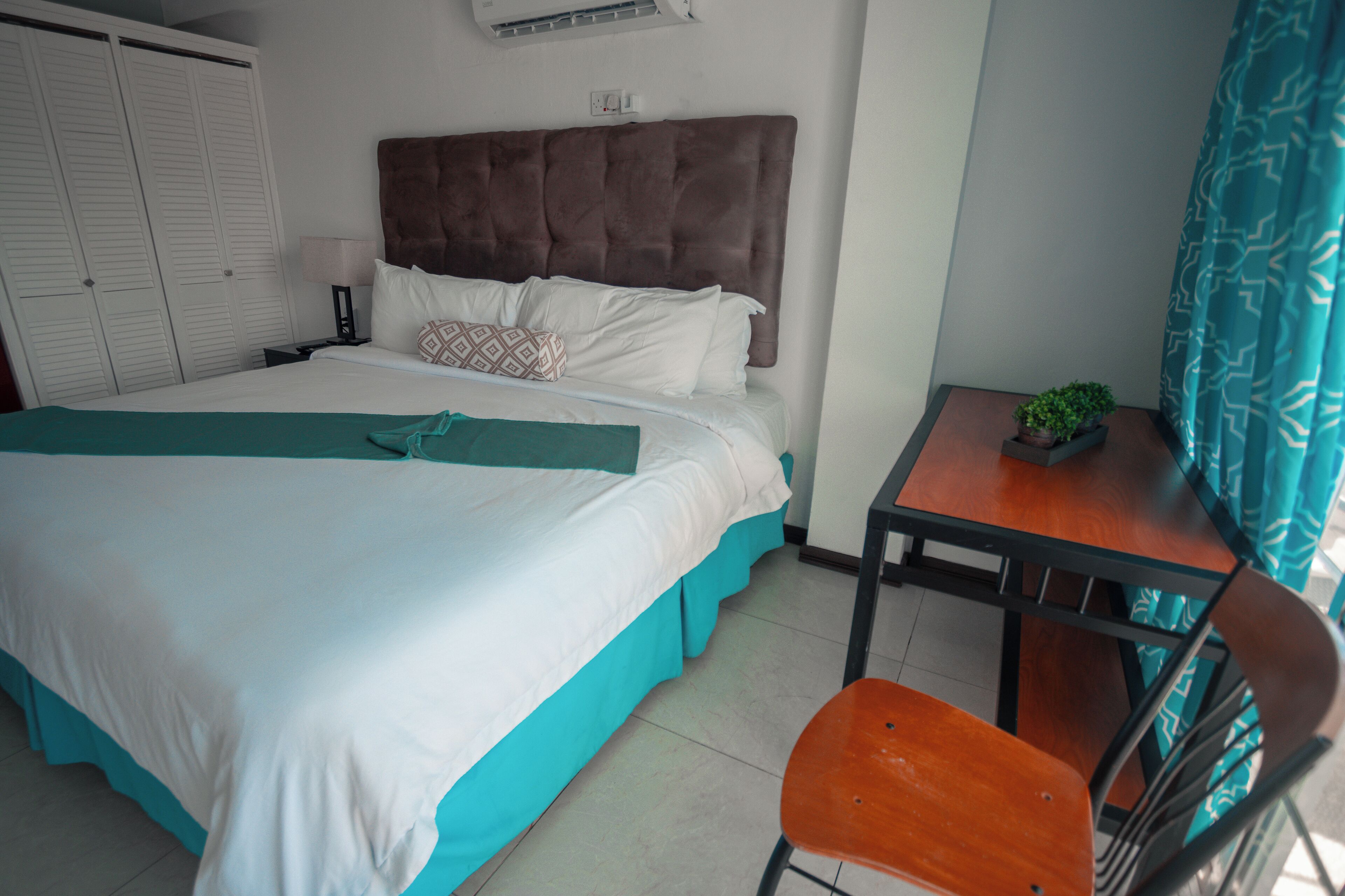 Une chambre d’hôtel comprenant un lit, un bureau, une chaise, une plante en pot et une armoire.