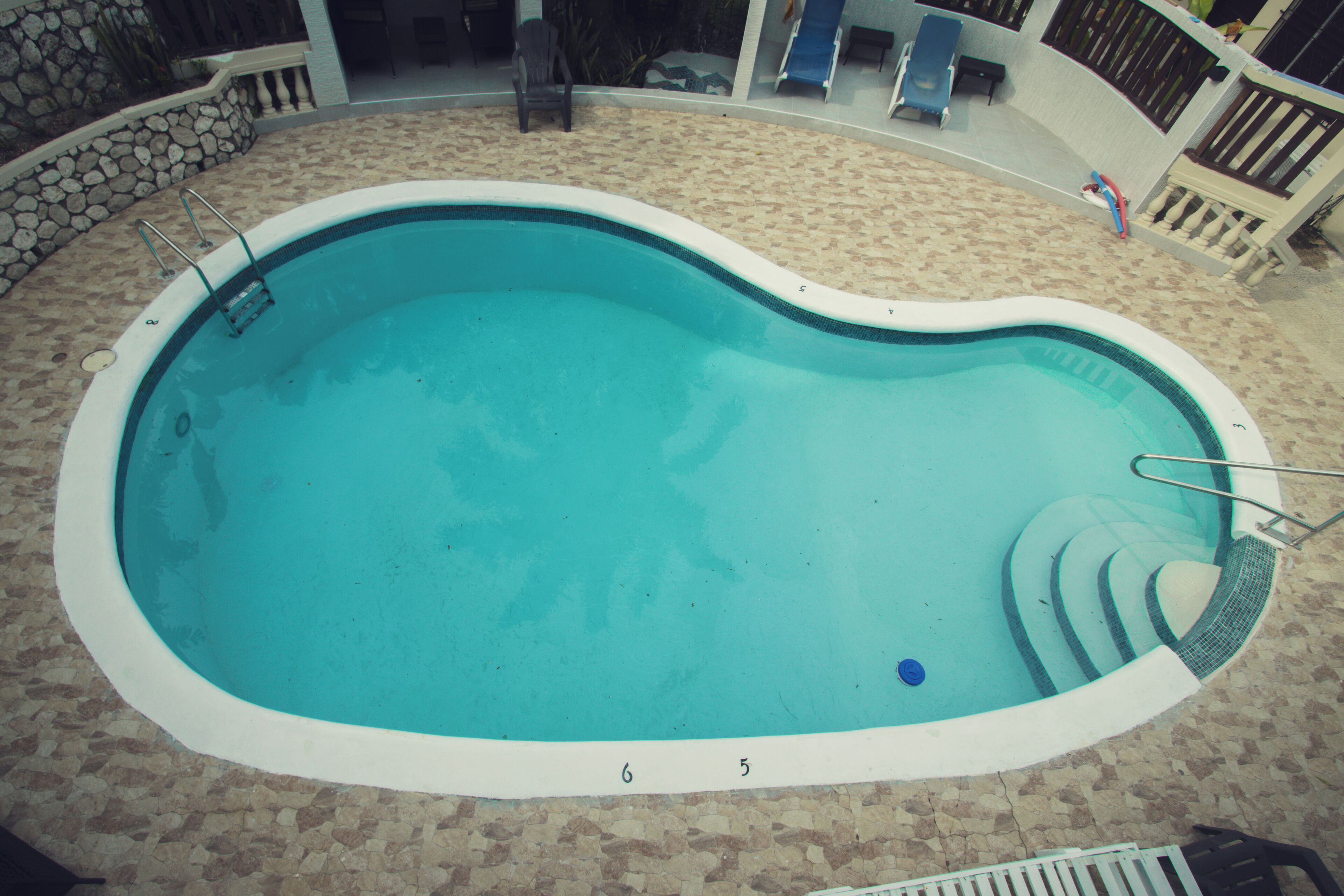Une piscine avec des marches permettant d’y accéder, entourée d’un mur en pierre et d’une terrasse carrelée.