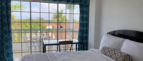 A hotel room with a bed, a balcony with a table and chairs, and a view of the outside.