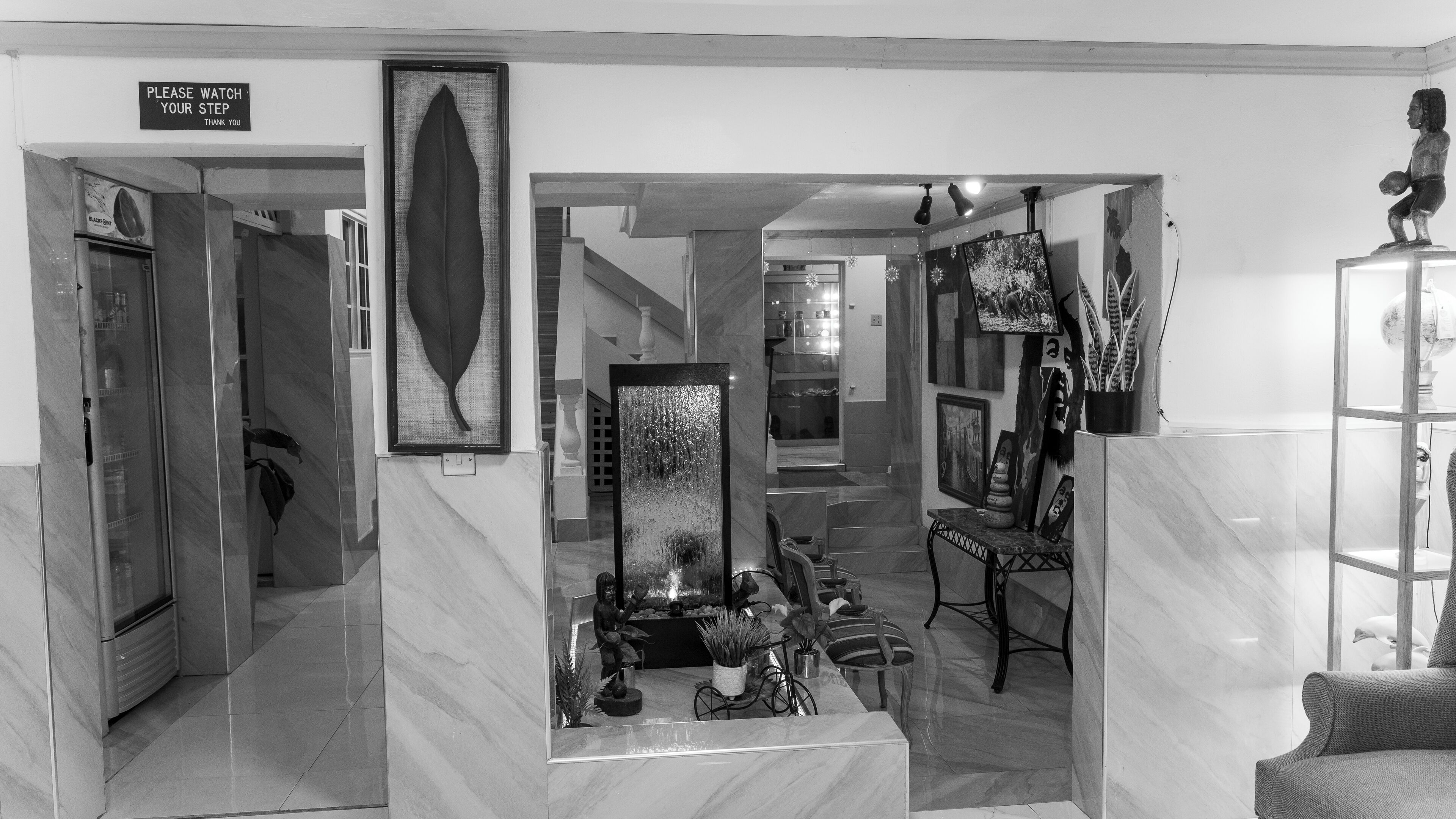 A lobby with a marble floor, a reception desk, a staircase, and a sign that reads 'PLEASE WATCH YOUR STEP THANK YOU'.