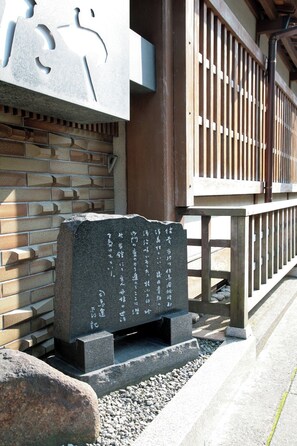 A stone monument with inscriptions, a brick wall, and a wooden fence. - Tsutaya Ryokan (Toyooka)