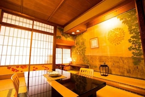 Een traditionele Japanse kamer met tatami vloeren, een lage tafel met kussen, en schuifdeuren met een bloemenprint.