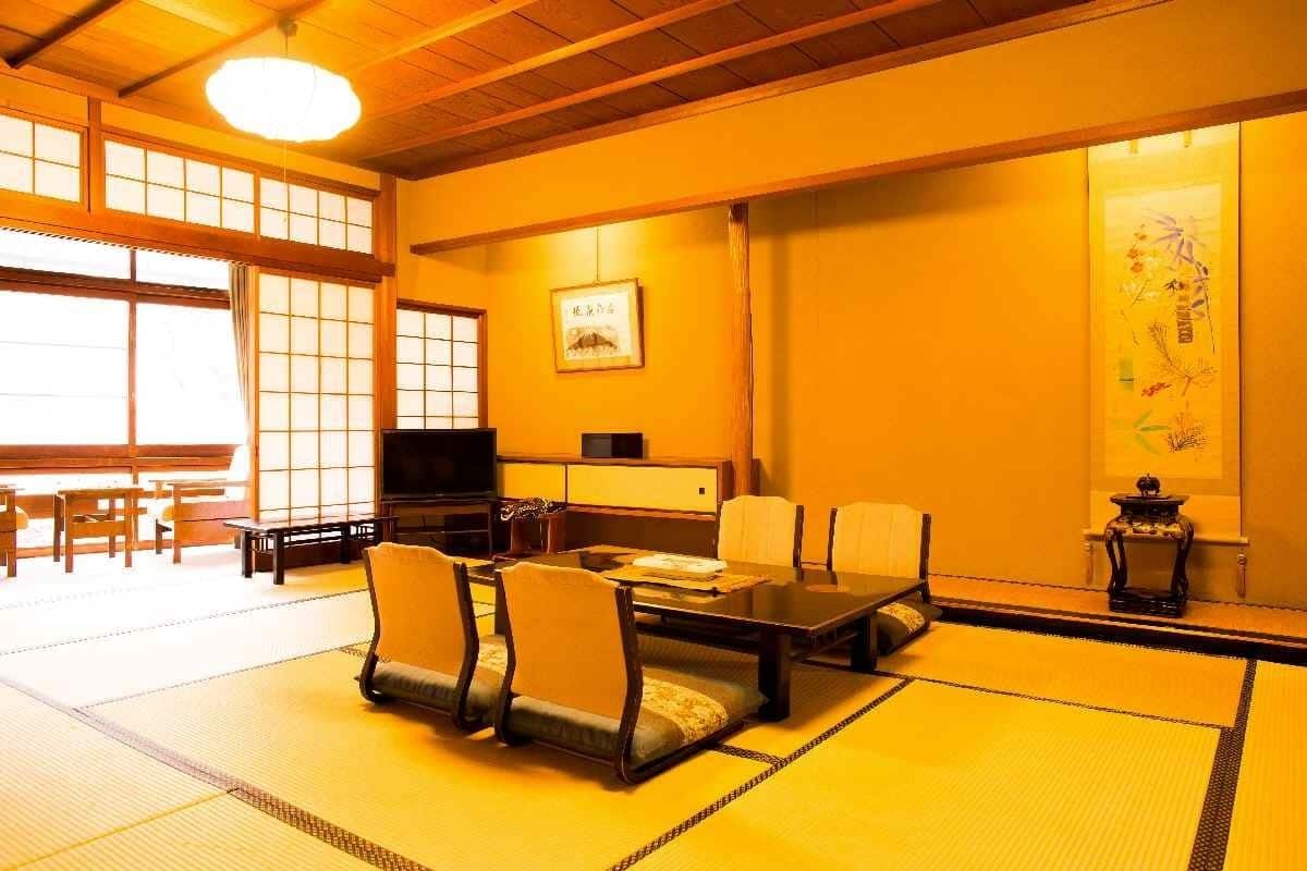 A traditional Japanese room with tatami flooring, a low table with chairs, a television, and a sliding door.