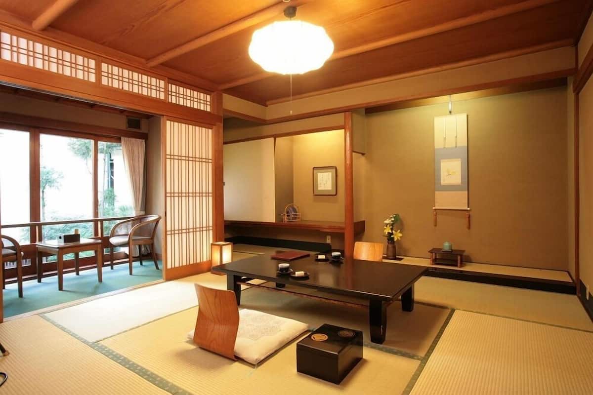 A traditional Japanese room with tatami flooring, a low table with tea set, sliding doors, and a view through a window.