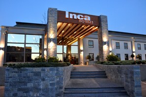 A hotel entrance with a sign reading "Inca Hotels," a modern facade, and a set of stairs leading up to the entrance. - Inca Hoteles (Los Andes)