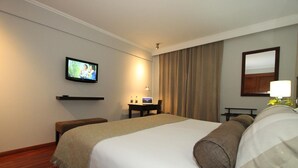 A hotel room with a large bed, a television mounted on the wall, a desk with a lamp, and a mirror.