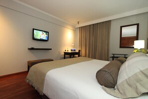 A hotel room with a large bed, a television mounted on the wall, a desk with a lamp, and a mirror.
