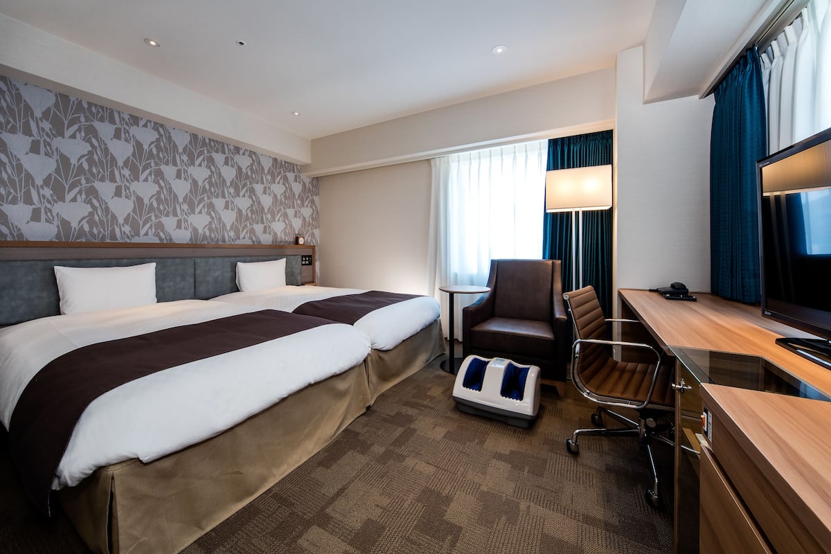 Habitación de hotel con dos camas, un escritorio, una silla, un sillón de masaje y un televisor.