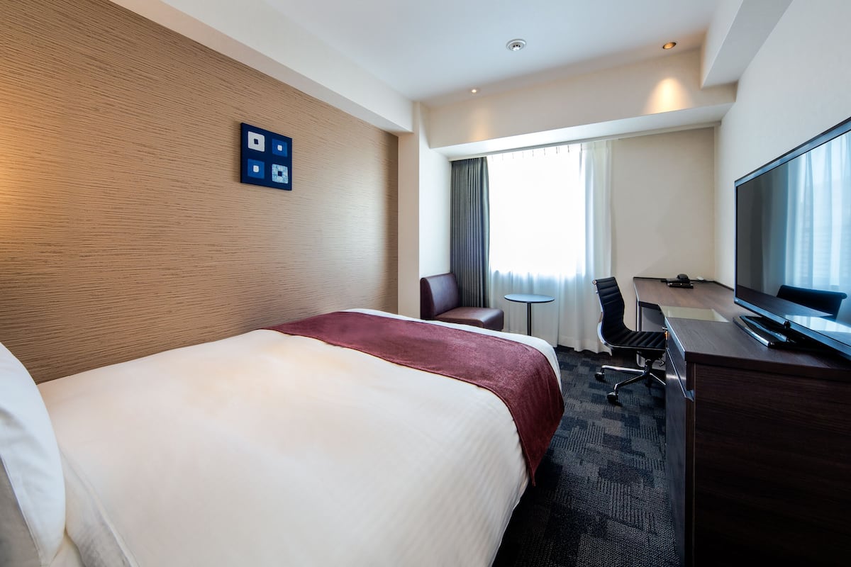 Una habitación de hotel con una cama grande, un escritorio con una silla, un televisor y una ventana con cortinas.