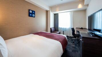 A hotel room with a large bed, a desk with a chair, a television, and a window with curtains.