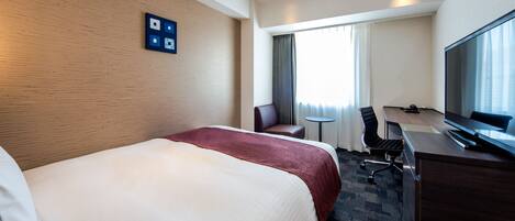 Quarto de hotel com uma cama grande, uma escrivaninha com cadeira, televisão e janela com cortinas.