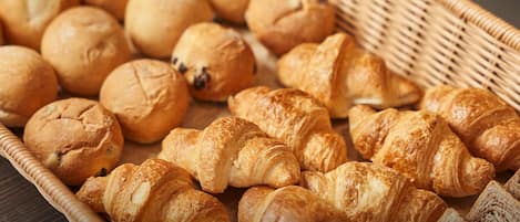 Una cesta de mimbre llena de panes variados, incluyendo cruasanes y hogazas redondas.