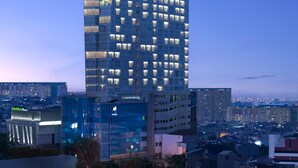 Un hotel moderno de gran altura con varios pisos, amplias ventanas y un llamativo logo 'HS' en la parte superior.