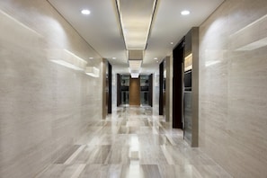 Un pasillo moderno y bien iluminado con pisos y paredes de mármol pulido, que conduce a una zona central con un revestimiento de pared de madera.