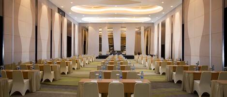 A conference room with rows of tables and chairs, a modern ceiling design, and a long table at the front.