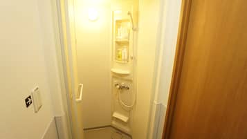 A narrow bathroom with a shower, a toilet, and a sink. There are toiletries on the shelves.