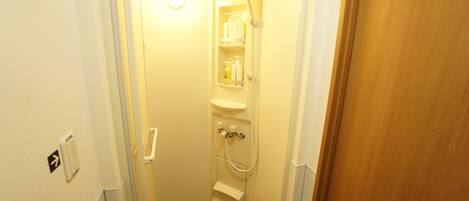 A narrow bathroom with a shower, a toilet, and a sink. There are toiletries on the shelves.