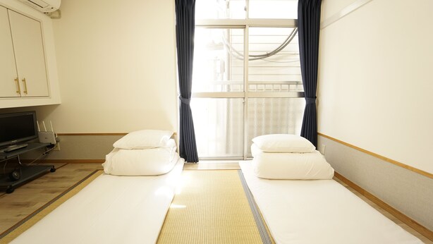 Una habitación de hotel con dos camas individuales, un televisor y una ventana con cortinas.