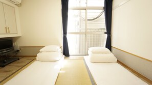 A hotel room with two single beds, a TV, and a window with curtains. - House Ikebukuro – Hostel (Tokyo)