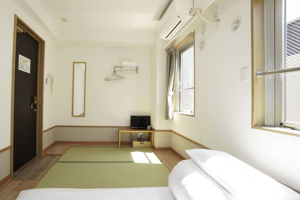 A hotel room with a bed, a small table, a TV, a window, and an air conditioning unit.