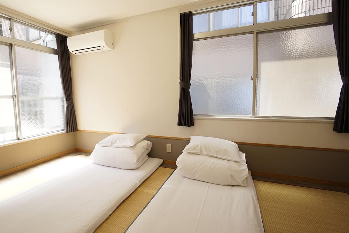 A hotel room with two single beds, a window with frosted glass, an air conditioning unit, and a wooden floor.