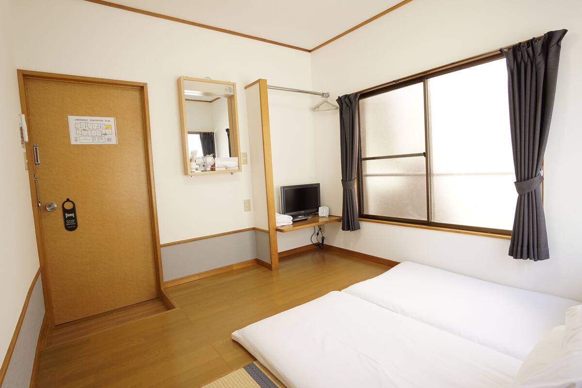 A hotel room with a bed, a desk with a computer, a mirror, and a window with curtains.