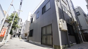 Una estrecha calle urbana con edificios modernos, una entrada vigilada y visible infraestructura eléctrica.