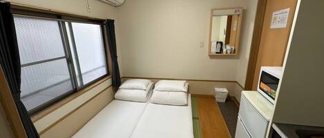 A compact room with a bed, a small kitchenette, a window with curtains, and a mirror.