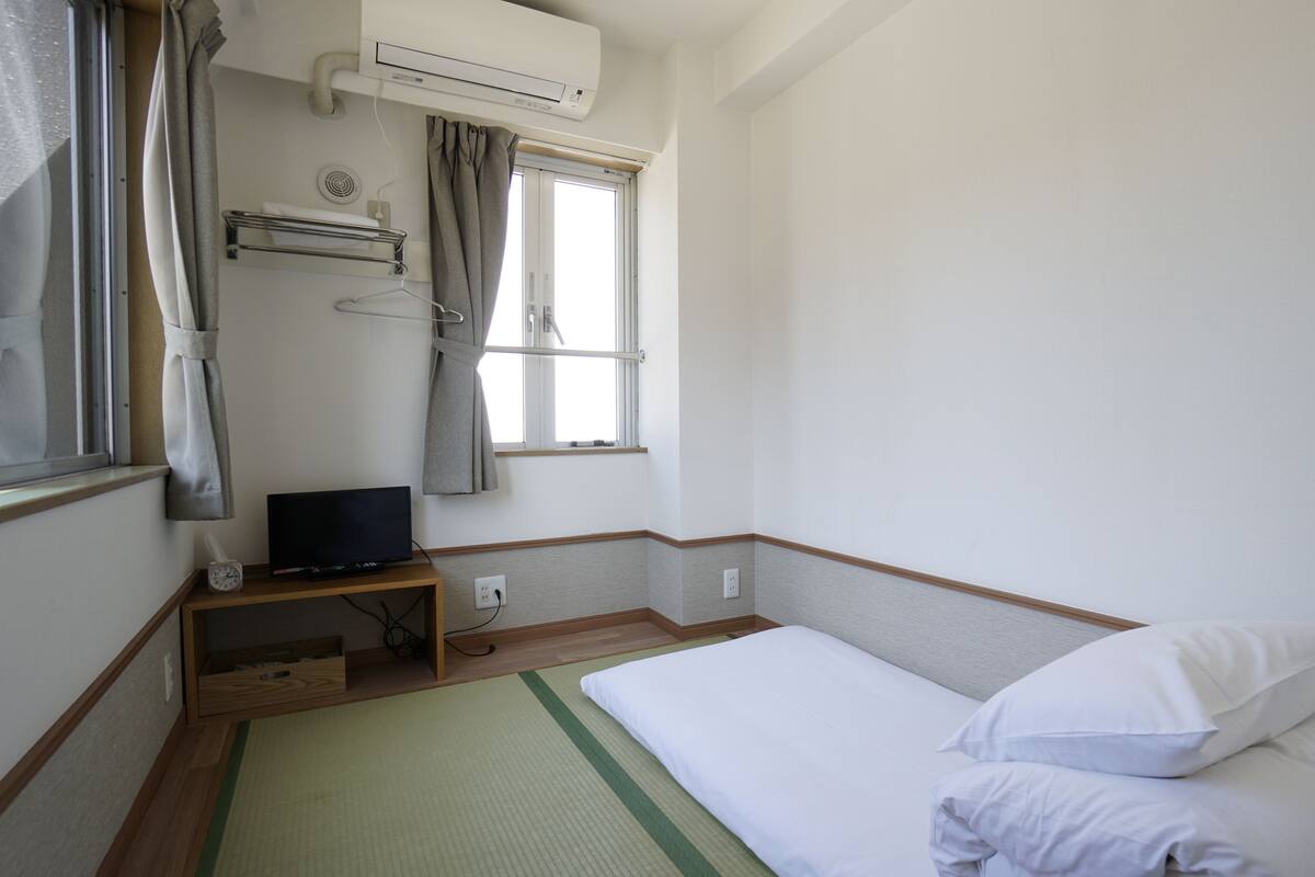 A hotel room with a bed, a TV, a window with curtains, and an air conditioning unit.