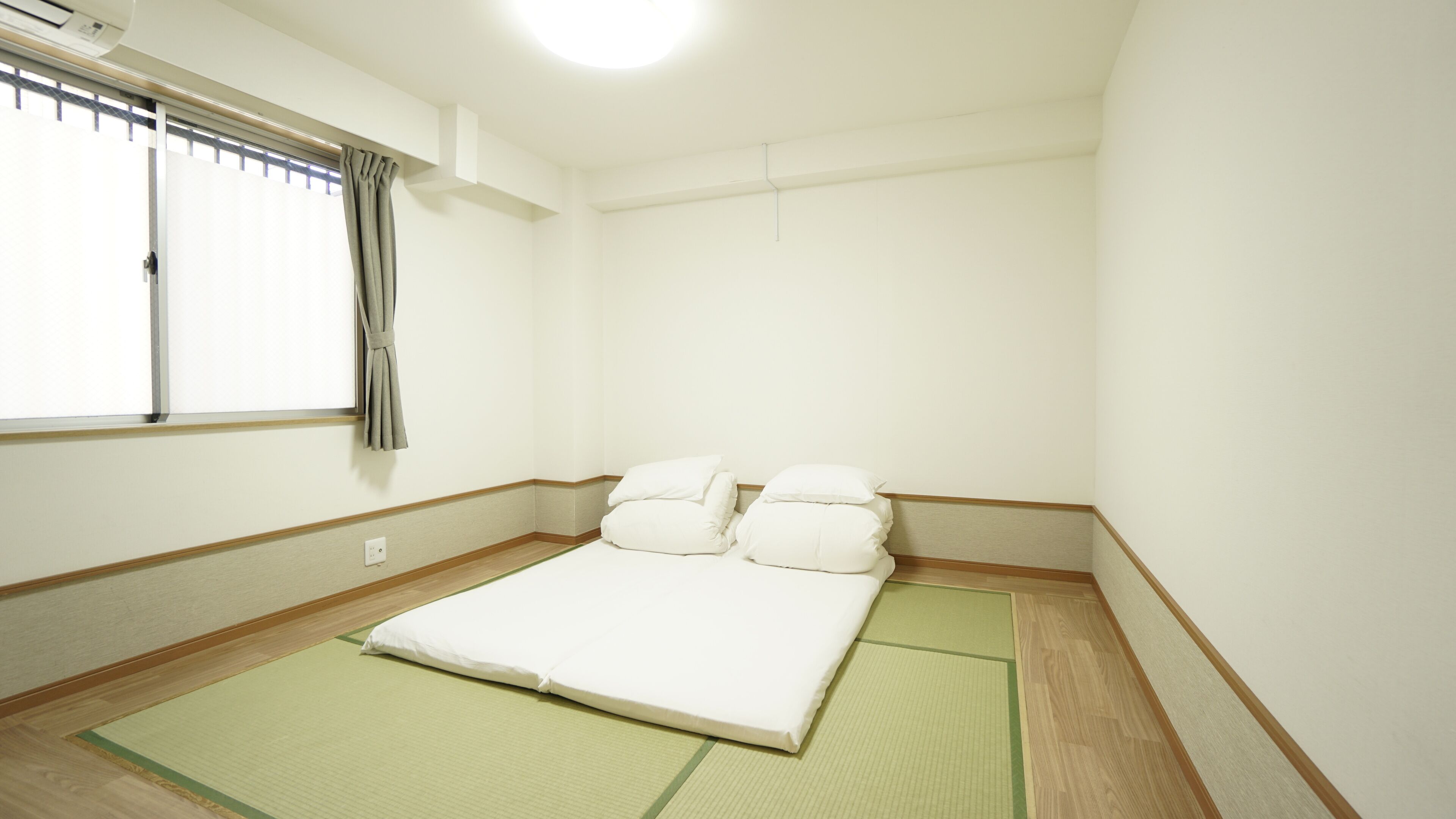 A room with a bed, pillows, a window with curtains, and tatami mats.