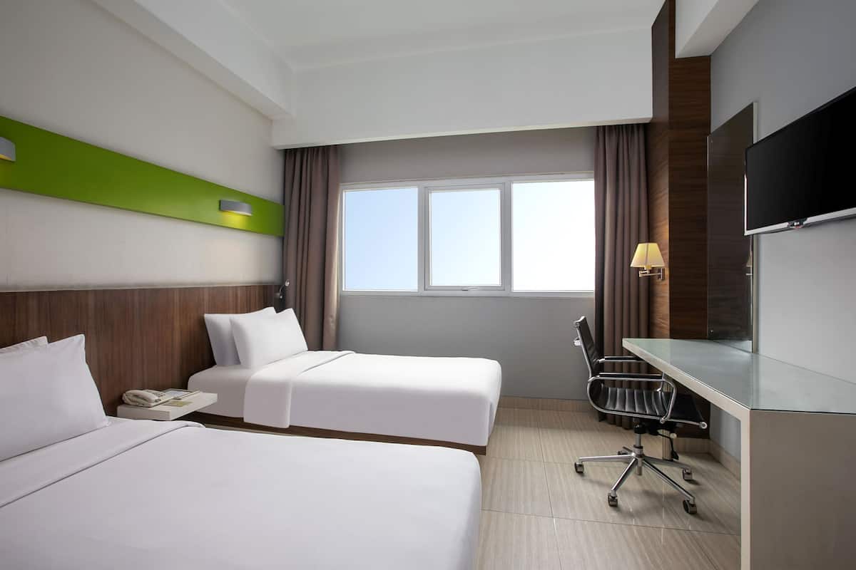 Quarto de hotel com duas camas, uma mesa, uma cadeira, uma televisão e uma janela com cortinas.