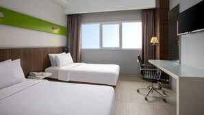 Quarto de hotel com duas camas, uma mesa, uma cadeira, uma televisão e uma janela com cortinas.