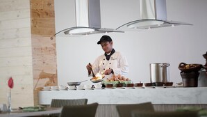 Um cozinheiro preparando alimentos em uma cozinha moderna com parede de detalhes em madeira e eletrodomésticos de aço inoxidável.
