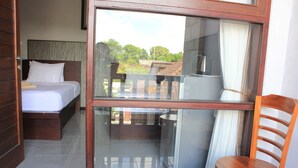 A hotel room with a bed, a wooden chair, a balcony with a view of the outdoors, and a refrigerator. - New Asta Graha Homestay (Kedonganan)