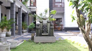 A courtyard with a central water feature, potted plants, and a building with balconies. - New Asta Graha Homestay (Kedonganan)